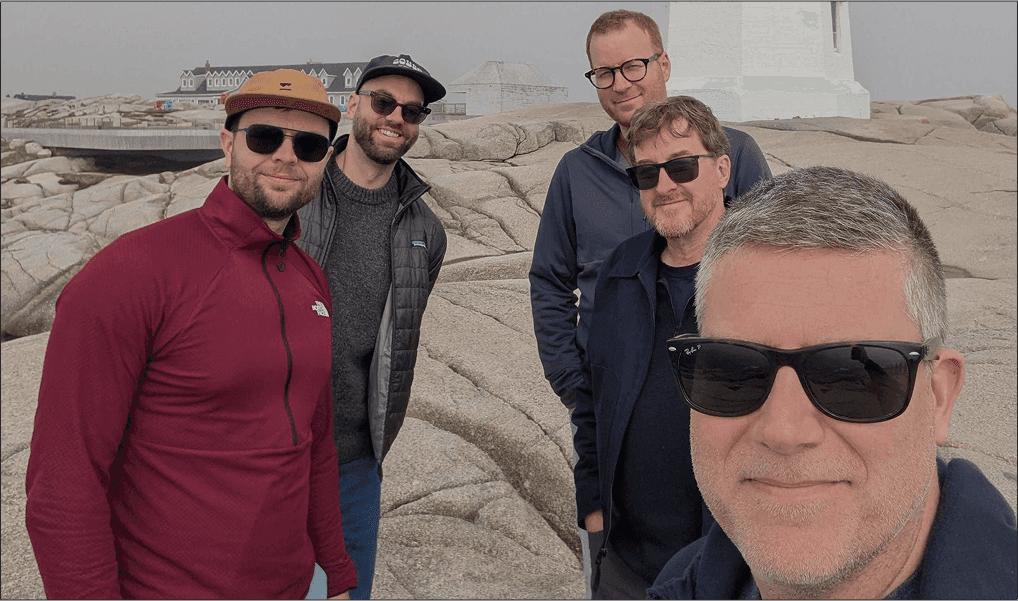 Five team members posing by a lighthouse on a rocky coastline.